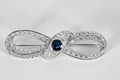 Broche Infini en platine, diamants et centre saphir.