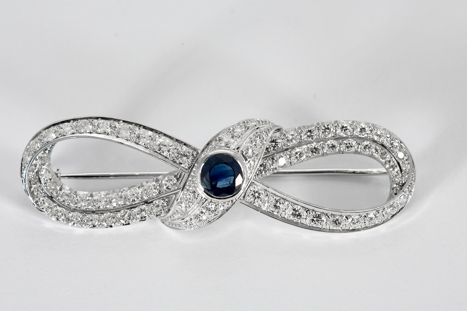 Broche Infini en platine, diamants et centre saphir.